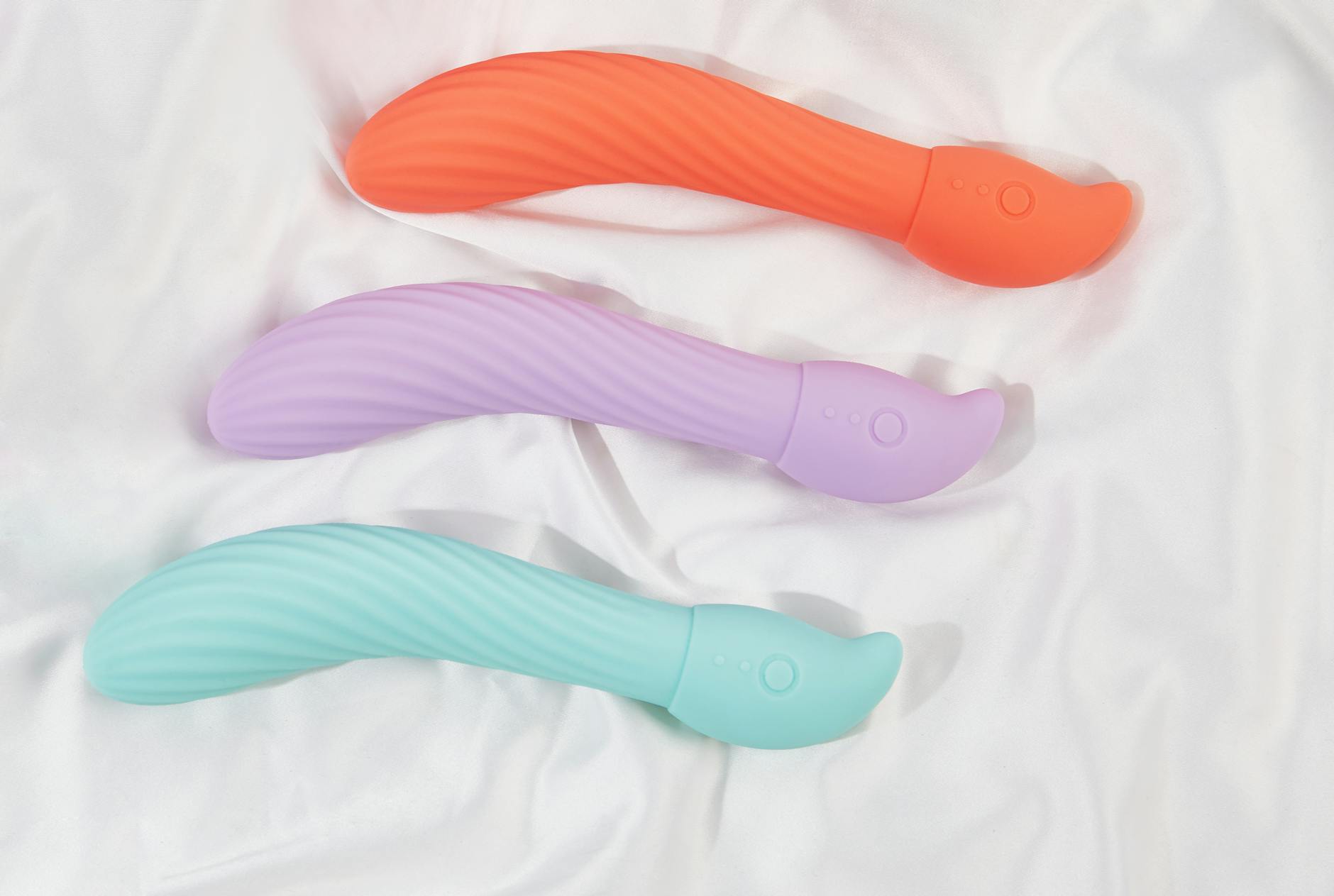 Mână ținând un vibrator colorat pe fundal minimalist, ilustrând plăcerea și auto-descoperirea de sine