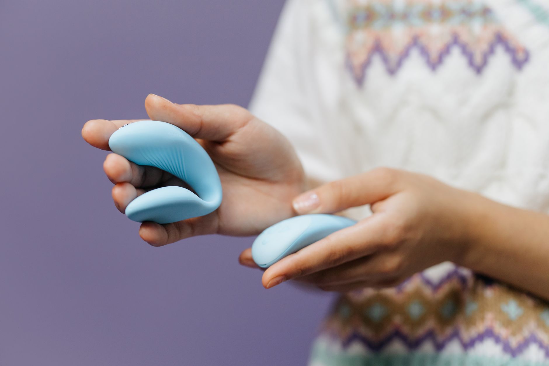 Mâini ținând un vibrator albastru elegant pe fundal violet