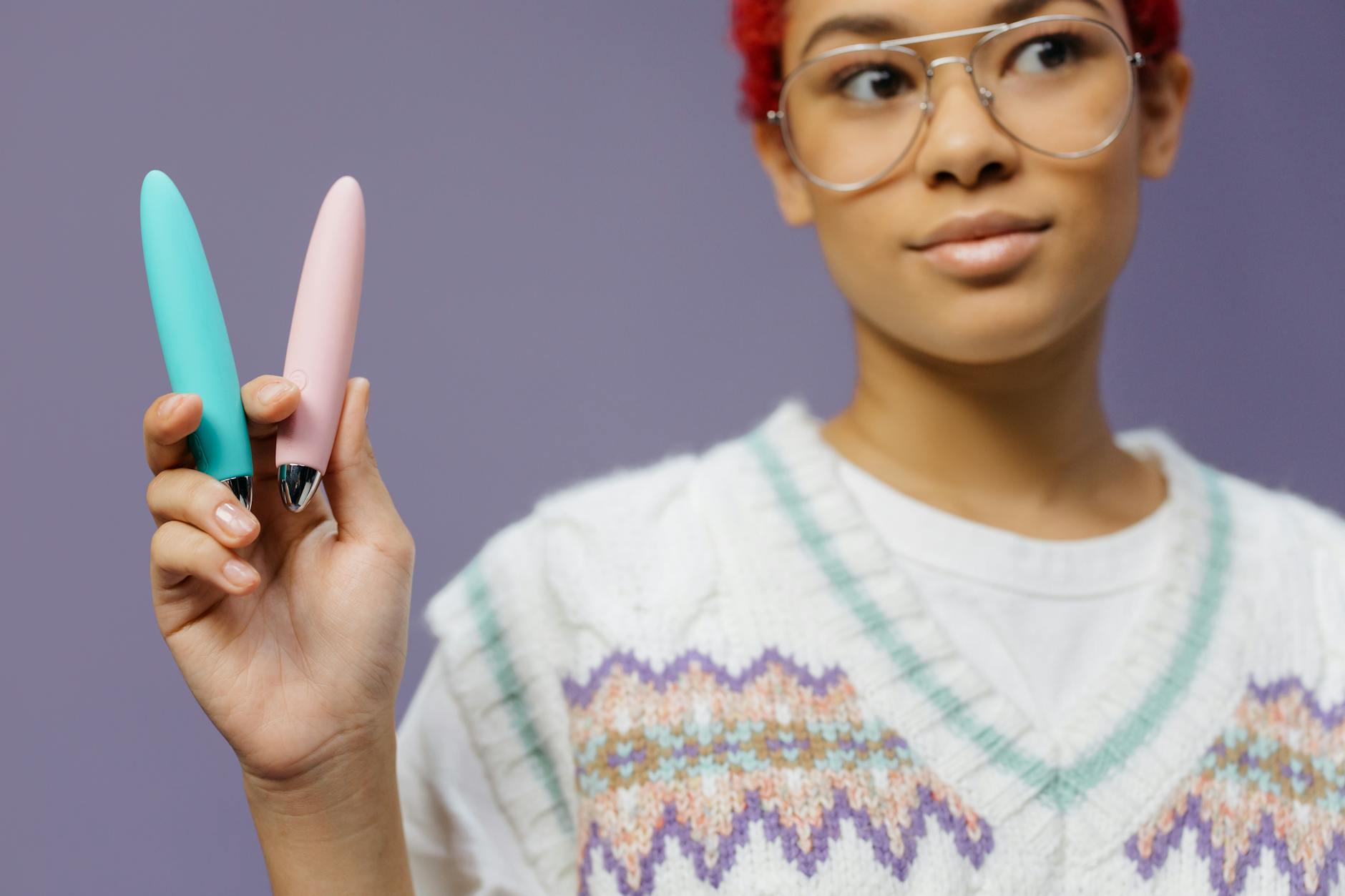 Două mâini ținând vibratoare roz și albastru pe un fundal pastel.