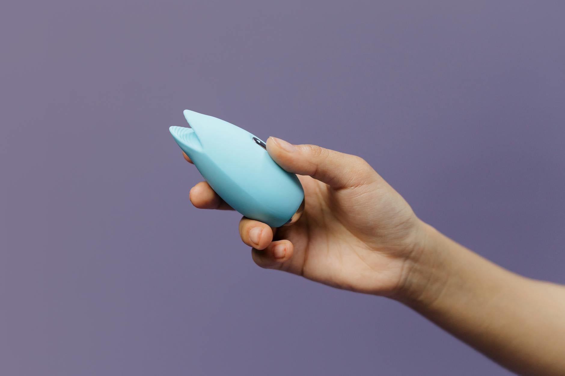 Un vibrator Lemon albastru ținut în mână pe fond violet solid, promovând plăcerea de sine și sexualitatea