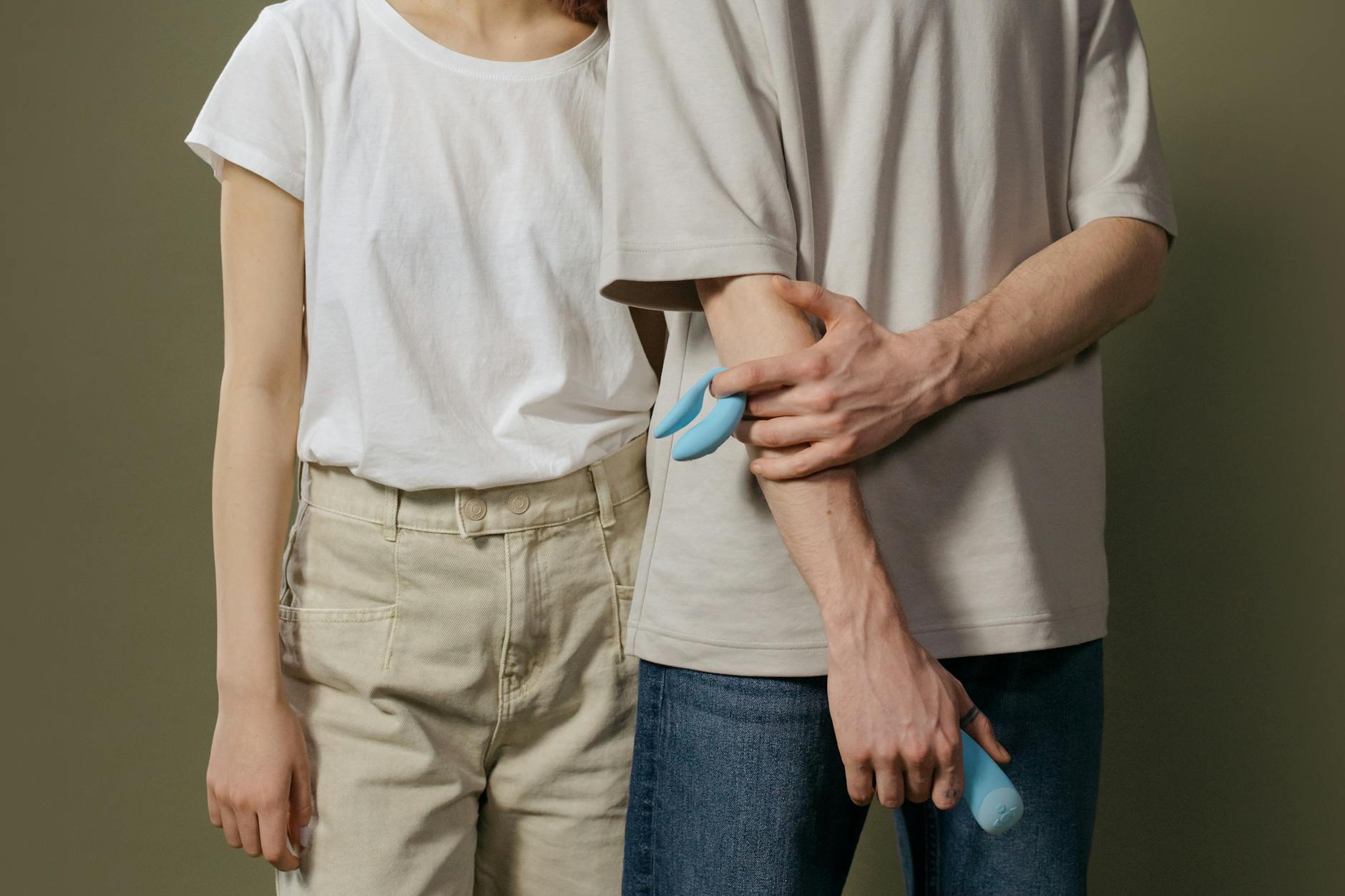 Un cuplu tânăr stând împreună în interior, ținând un vibrator albastru, simbolizând intimitatea modernă.