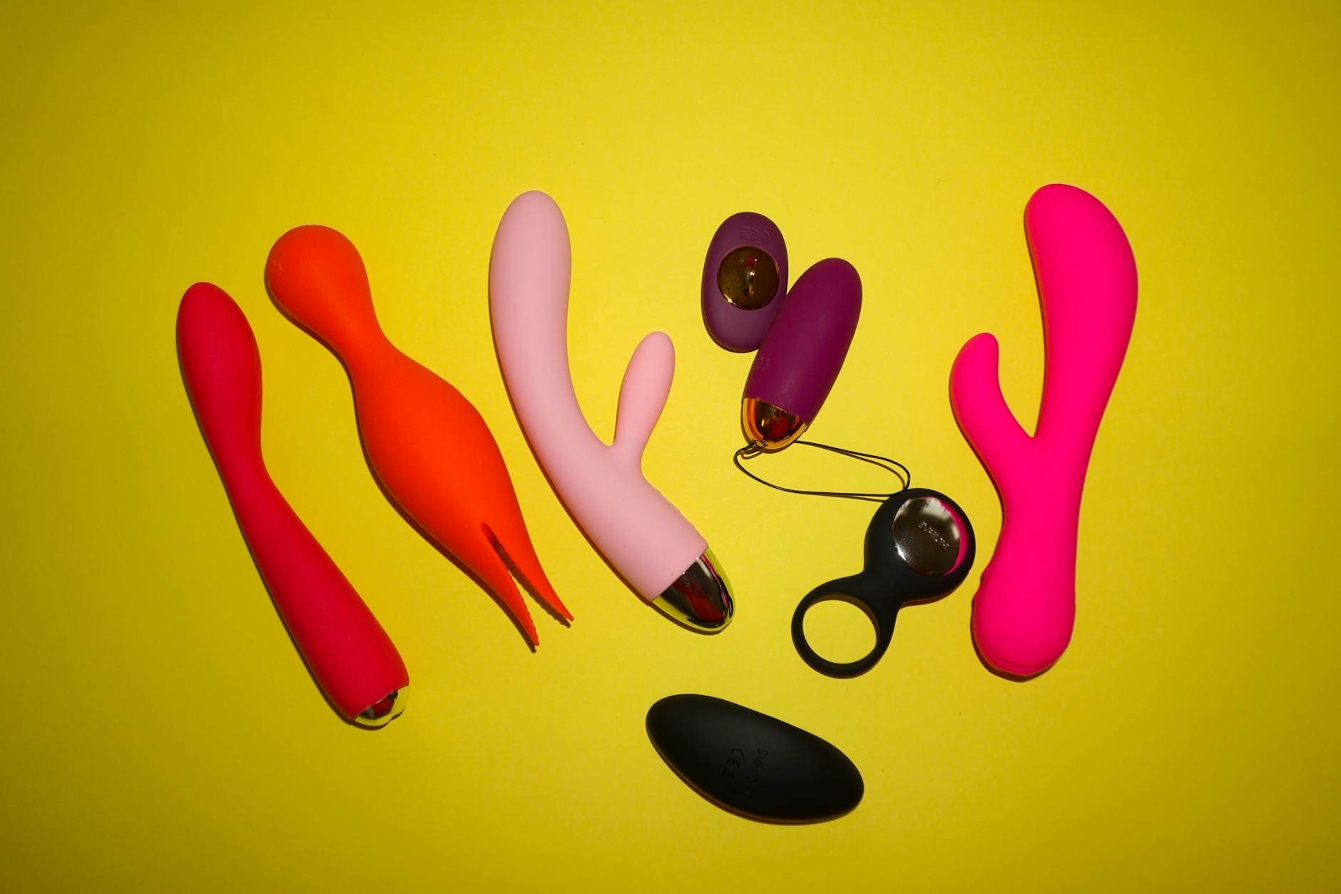 Vibratoare colorate expuse pe fundal galben intens, simbolizând modernitatea și diversitatea în intimitate