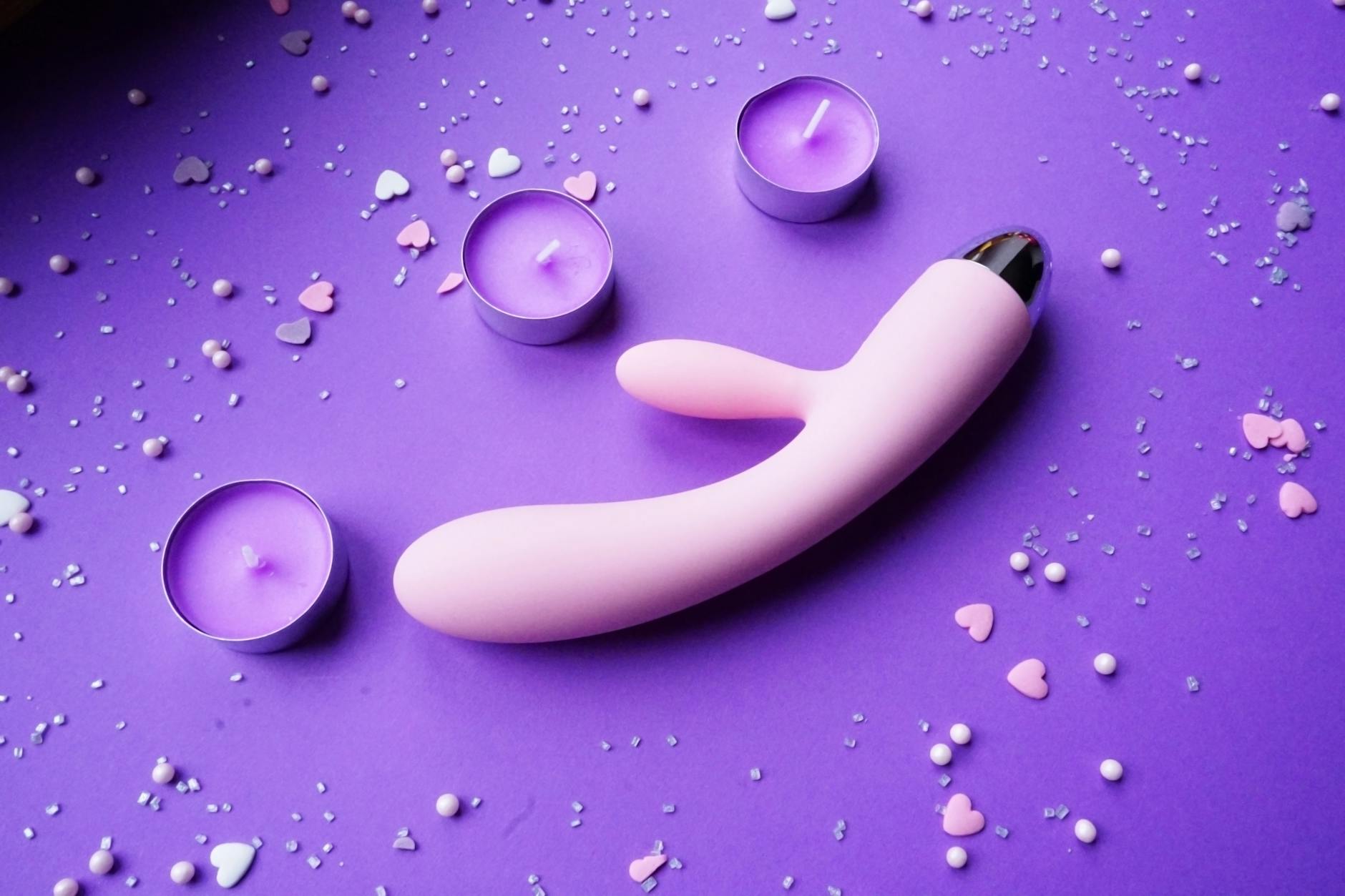 Vibratorin roz pe fundal mov cu confetti în formă de inimă și lumânări